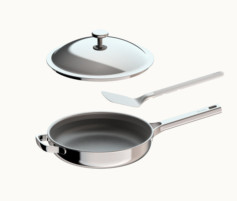 Stainless steel frying pan with a textured interior, a matching lid, and a metal spatula.