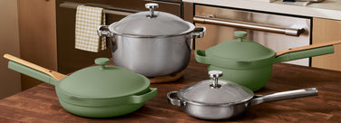Set of green and silver cookware on a wooden surface with kitchen cabinets in the background.