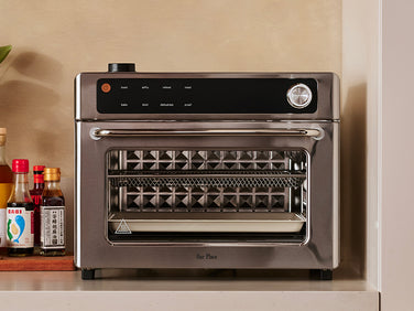 Stainless steel toaster oven on a kitchen counter with bottles in the background