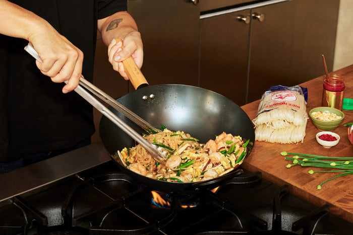 A hand holding a wok with food cooking inside of it