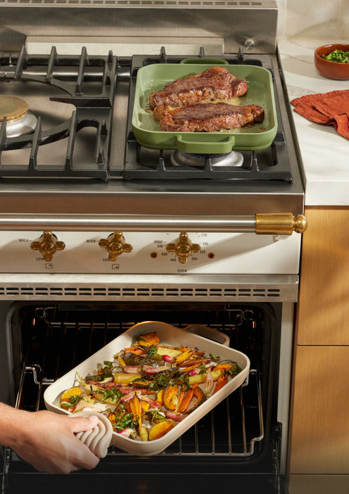 Steak cooking on a green Mini Griddle Pan on the stove and roasted vegetables cooking on a beige Mini Griddle Pan in the oven