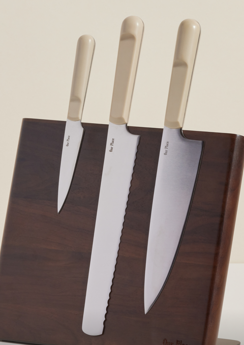 A set of three beige-handled kitchen knives—paring, bread, and chef’s knives—displayed on a dark wooden magnetic knife block, against a light background.