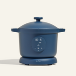 A modern blue electric cooking pot with a digital timer display on the front, a round lid on top, and short handles on each side, placed against a plain light background.