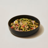 A black bowl filled with yellow rice mixed with shredded meat, green olives, green beans, and diced red vegetables.
