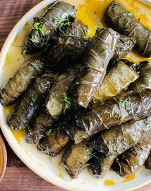 A plate of stuffed grape leaves arranged in a pile, garnished with fresh herbs and drizzled with oil.