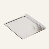 A rectangular, stainless steel tray with a raised edge on one side, shown on a plain light background.