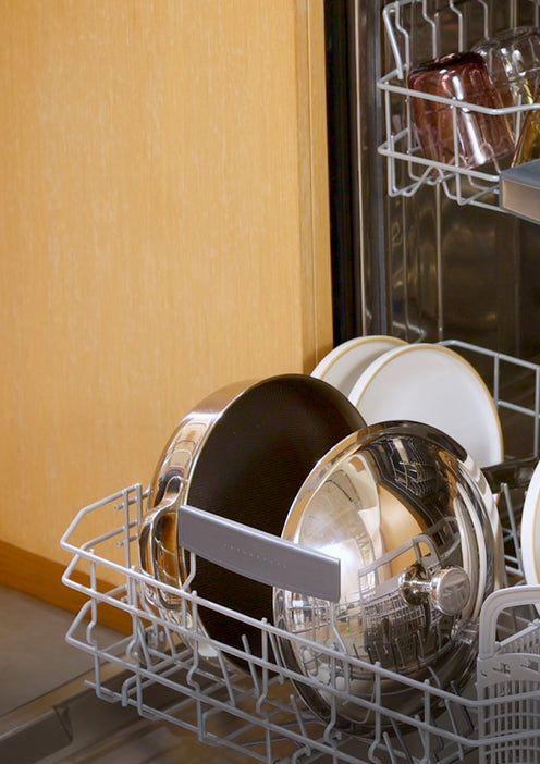 An open dishwasher with neatly arranged clean dishes, including pots, pans, bowls, and glasses, visible on the racks inside a kitchen.