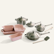 The Titanium Pro Cookware + Bakeware Set includes stainless steel pots and pans with lids, pink ceramic nonstick baking dishes, a loaf pan, spatula, and wooden spoon—all arranged on a plain surface.