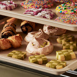 Assorted pastries including croissants, meringues, and checkered cookies on a baking tray.