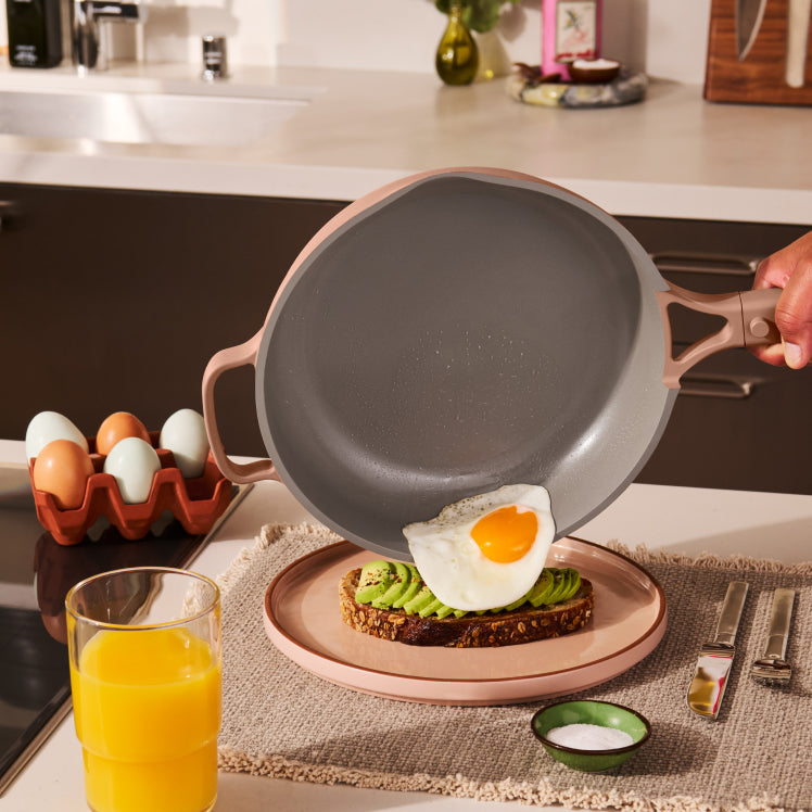 A fried egg sliding off a Ceramic Nonstick Always Pan onto avocado toast.