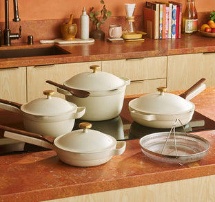 Set of white cookware with gold handles on a kitchen counter.