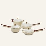 The Cookware Set features four cream-colored pieces with wooden handles and gold knobs: two pans, an Always Pan saucepan with lid, and a pot with lid, all displayed on a light background.