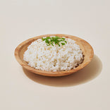 A wooden bowl filled with white rice, topped with chopped green onions, on a light-colored background.